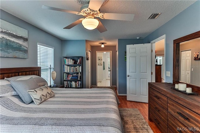 bedroom with wood-type flooring, connected bathroom, a textured ceiling, and ceiling fan