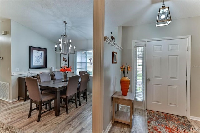 dining area with a chandelier, light hardwood / wood-style floors, vaulted ceiling, and a textured ceiling