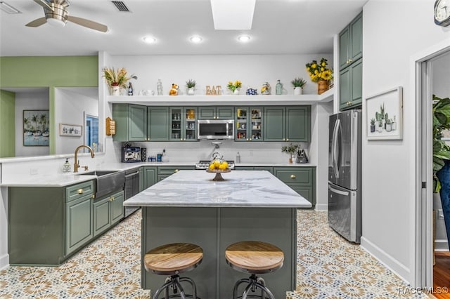 kitchen with a skylight, a peninsula, stainless steel appliances, green cabinets, and a sink