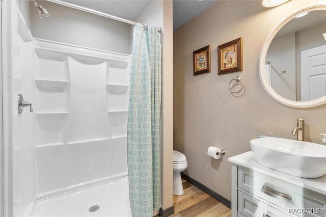 bathroom with curtained shower, toilet, wood finished floors, vanity, and baseboards