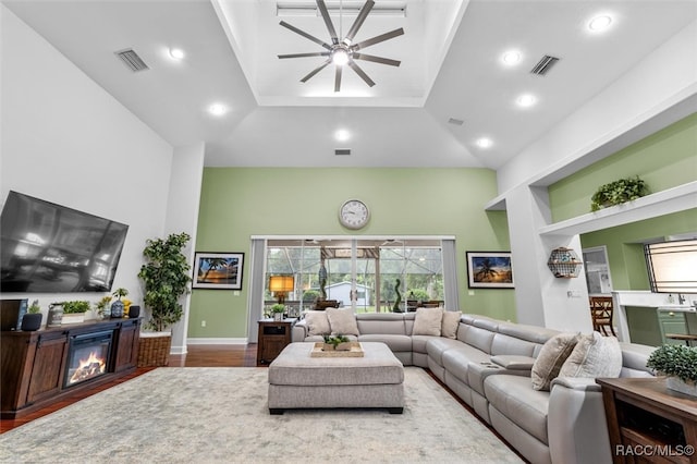 living room featuring built in shelves, a glass covered fireplace, visible vents, and wood finished floors