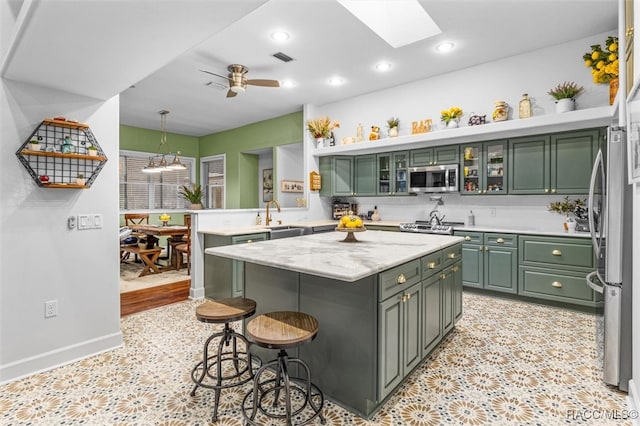 kitchen with a breakfast bar area, stainless steel appliances, a kitchen island, a sink, and green cabinetry