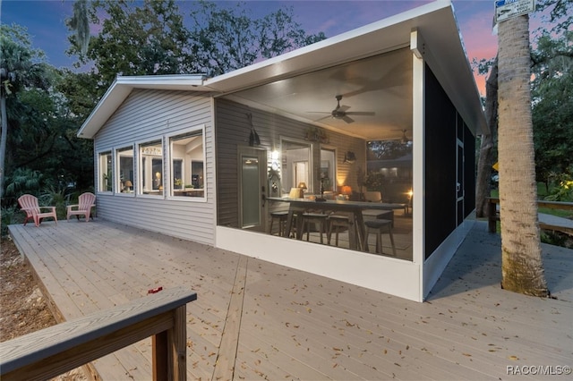 deck at dusk with a sunroom, ceiling fan, and a patio