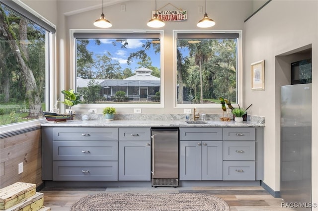 kitchen with a sink, light wood finished floors, gray cabinets, and light stone countertops