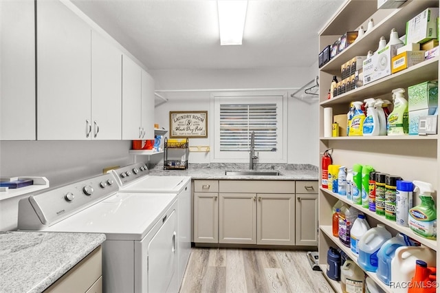 clothes washing area with light wood-type flooring, cabinet space, a sink, and independent washer and dryer