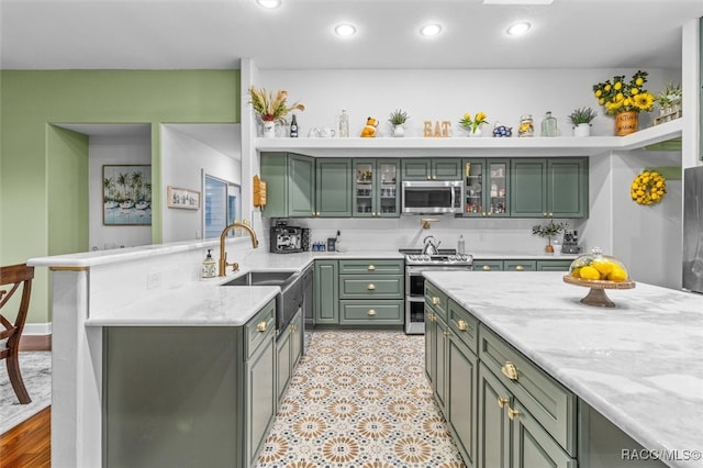 kitchen featuring recessed lighting, appliances with stainless steel finishes, a sink, green cabinetry, and a peninsula