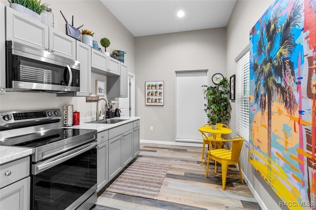 kitchen featuring gray cabinets, stainless steel appliances, light countertops, light wood-style floors, and a sink