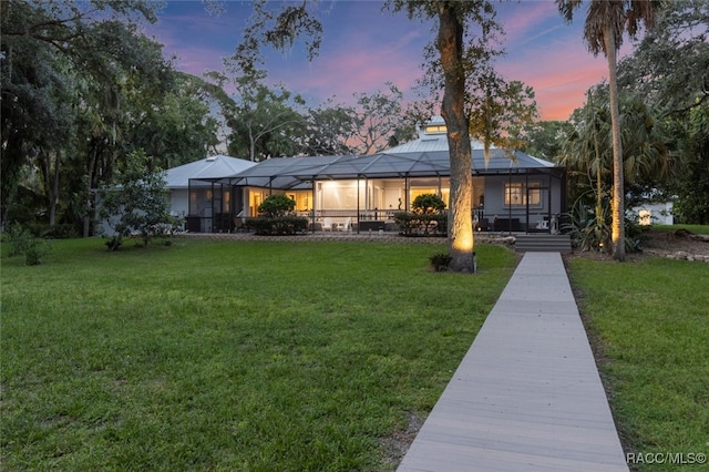 back of house at dusk featuring a lanai and a lawn