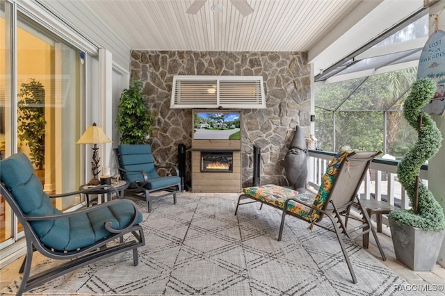 sunroom / solarium with plenty of natural light, an outdoor stone fireplace, and ceiling fan