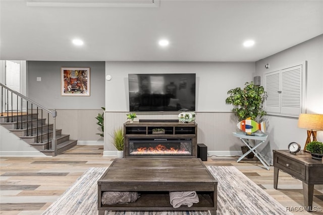 living area with stairway, a glass covered fireplace, wood finished floors, and wainscoting