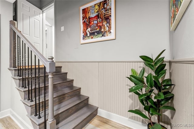 stairs with a wainscoted wall, wood finished floors, and baseboards