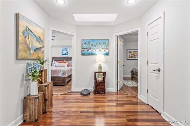 corridor with recessed lighting, a skylight, wood finished floors, and baseboards