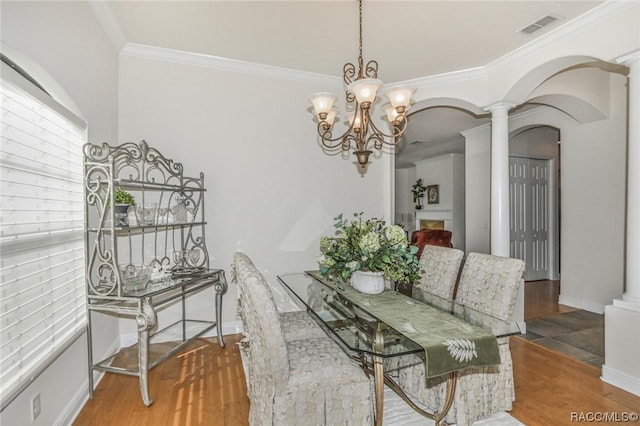 dining space with crown molding, decorative columns, a chandelier, and hardwood / wood-style flooring