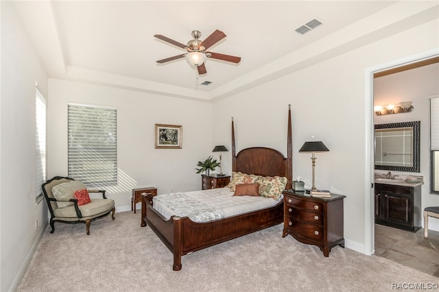 bedroom with sink, light colored carpet, ceiling fan, a tray ceiling, and ensuite bath