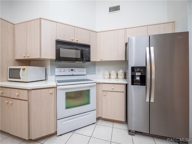 kitchen with light tile patterned flooring, white appliances, and light brown cabinets