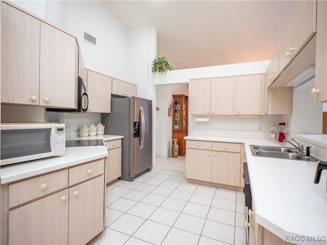 kitchen featuring a towering ceiling, stainless steel refrigerator with ice dispenser, light brown cabinetry, sink, and light tile patterned flooring