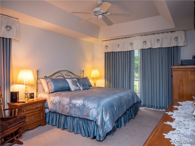 carpeted bedroom featuring ceiling fan and a tray ceiling