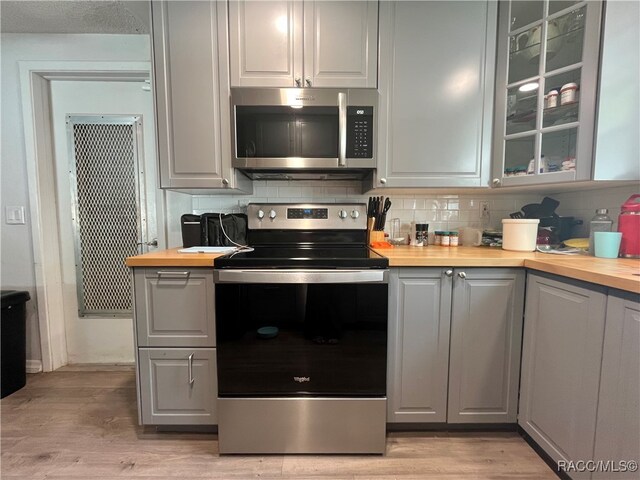 kitchen with light hardwood / wood-style flooring, wooden counters, backsplash, gray cabinets, and appliances with stainless steel finishes