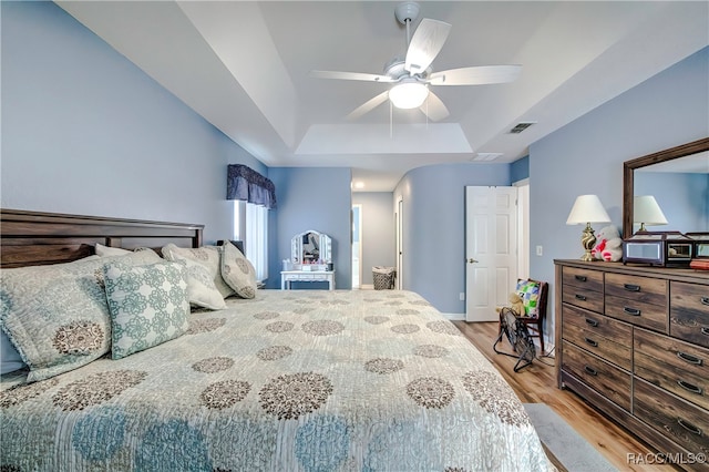 bedroom with a raised ceiling, light hardwood / wood-style flooring, and ceiling fan