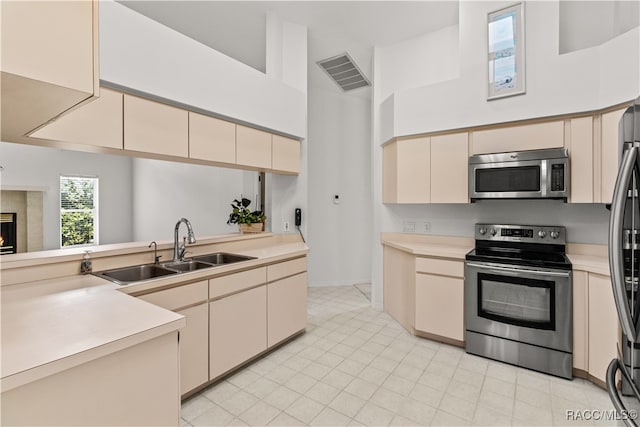 kitchen featuring cream cabinetry, sink, stainless steel appliances, and high vaulted ceiling