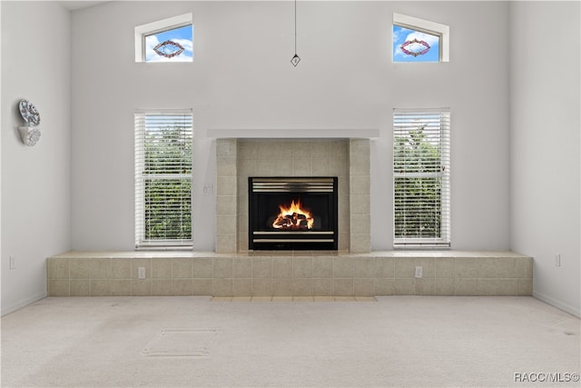 unfurnished living room featuring carpet, a high ceiling, a tile fireplace, and a wealth of natural light