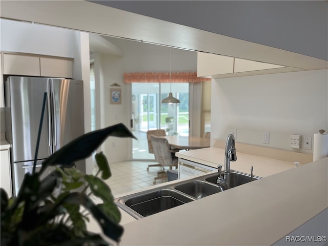 kitchen with stainless steel fridge, white cabinetry, hanging light fixtures, and sink