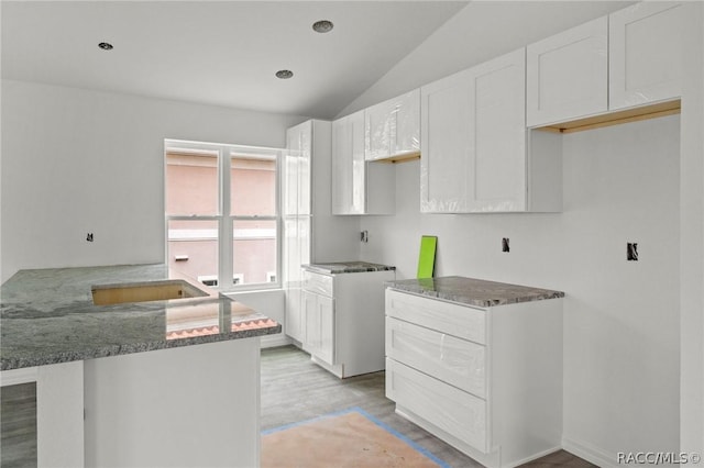 kitchen featuring stone countertops, white cabinetry, kitchen peninsula, and vaulted ceiling