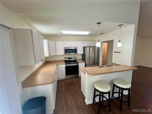 kitchen featuring white cabinets, dark wood-style floors, appliances with stainless steel finishes, a breakfast bar, and a sink