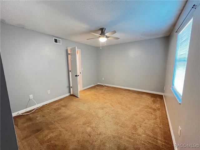 spare room featuring carpet, ceiling fan, a textured ceiling, and a wealth of natural light