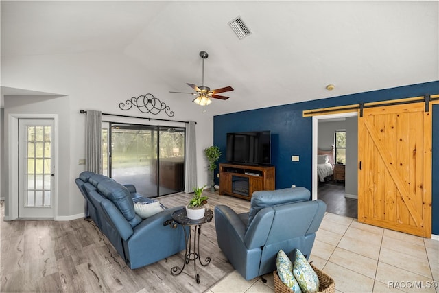 living room with ceiling fan, a barn door, light hardwood / wood-style floors, and vaulted ceiling