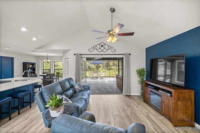 living room with ceiling fan with notable chandelier, lofted ceiling, sink, and light hardwood / wood-style flooring