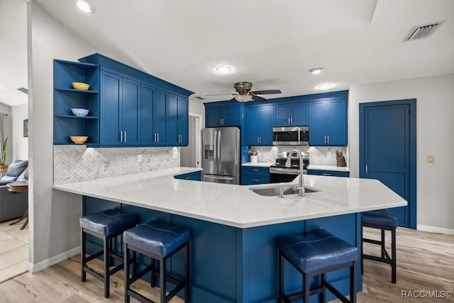 kitchen with blue cabinets, sink, a breakfast bar area, appliances with stainless steel finishes, and kitchen peninsula