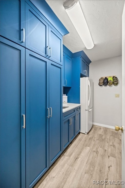 kitchen featuring white fridge, blue cabinetry, a textured ceiling, and light wood-type flooring