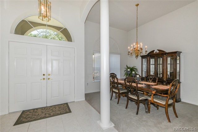 entryway with decorative columns, high vaulted ceiling, light colored carpet, and a notable chandelier