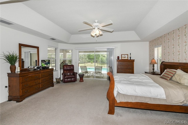 bedroom featuring a tray ceiling, access to exterior, ceiling fan, and light colored carpet