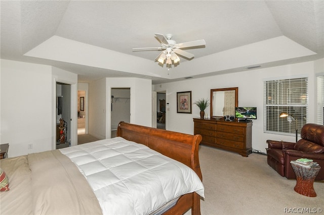 bedroom with a tray ceiling, light carpet, ceiling fan, and a spacious closet