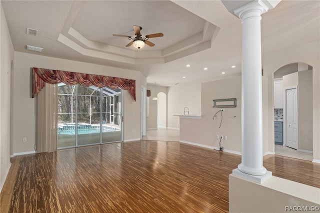 unfurnished living room featuring hardwood / wood-style floors, a tray ceiling, ceiling fan, and decorative columns