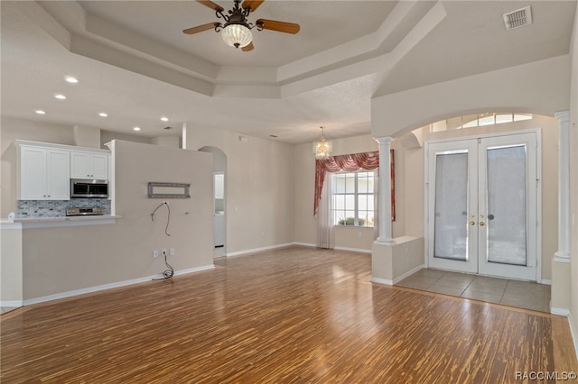 foyer entrance with ceiling fan with notable chandelier, light wood-type flooring, a tray ceiling, and french doors