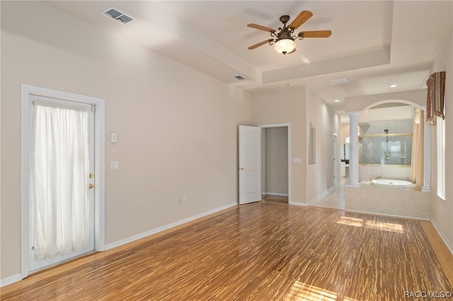 unfurnished room featuring hardwood / wood-style flooring, decorative columns, a tray ceiling, and ceiling fan