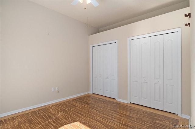 unfurnished bedroom with hardwood / wood-style flooring, ceiling fan, and multiple closets