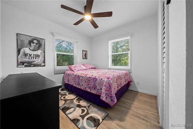 bedroom featuring ceiling fan, multiple windows, baseboards, and wood finished floors