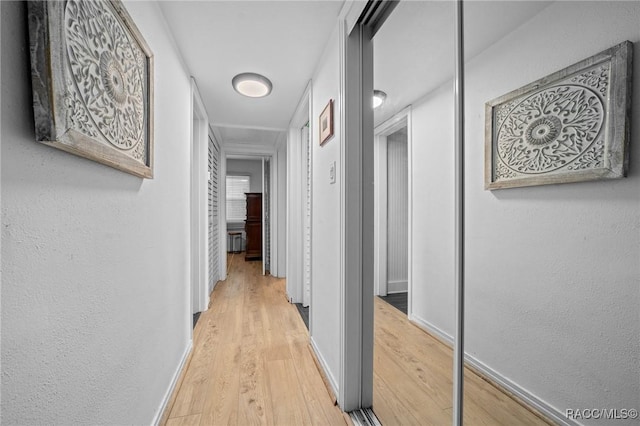 hall featuring light wood finished floors, baseboards, and a textured wall