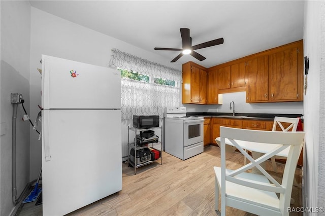 kitchen featuring white appliances, dark countertops, light wood-style flooring, brown cabinets, and a sink