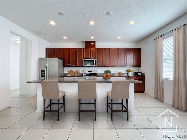 kitchen featuring a kitchen bar, a kitchen island with sink, stainless steel appliances, and a textured ceiling