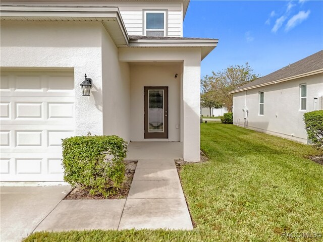 view of exterior entry with a lawn and a garage