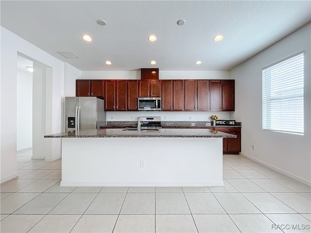 kitchen with dark stone counters, a center island with sink, sink, a textured ceiling, and stainless steel appliances