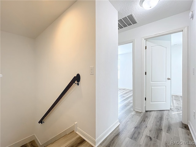 hall with light hardwood / wood-style floors and a textured ceiling