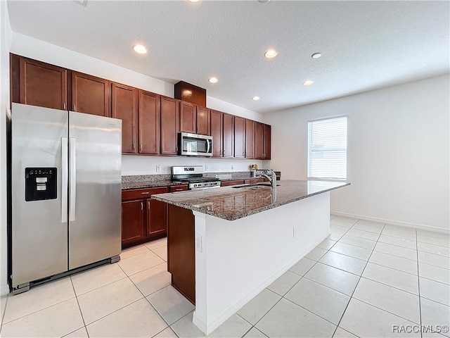 kitchen with a kitchen island with sink, dark stone counters, sink, a textured ceiling, and stainless steel appliances