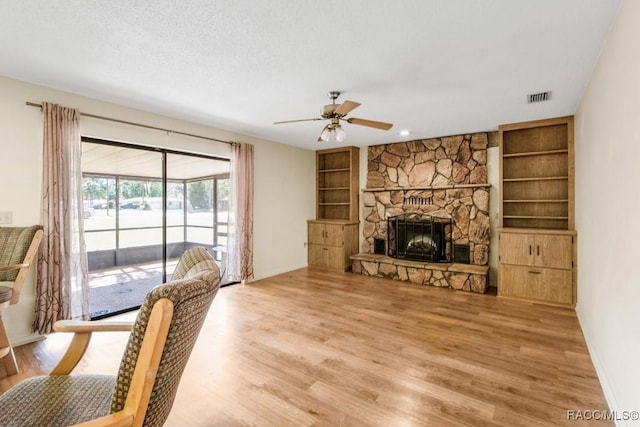 living room with hardwood / wood-style floors, ceiling fan, a stone fireplace, and a textured ceiling