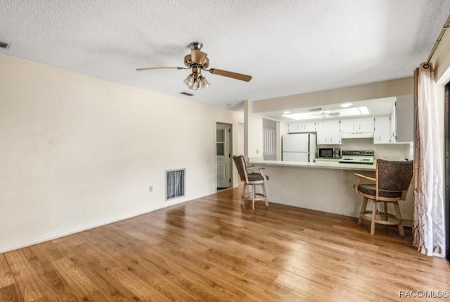 unfurnished living room with a textured ceiling, light wood-type flooring, and ceiling fan